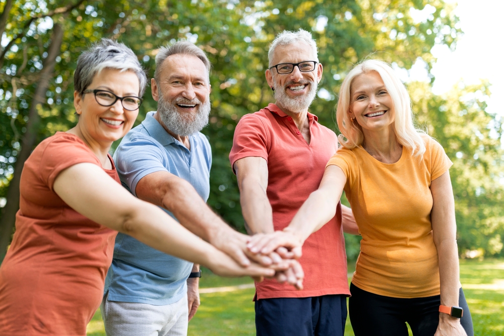 Family Dental Care for Teens, Dentist Prescott AZ Group of cheerful senior people stacking hands after sport workout outdoors, happy mature men and women joining palms and looking at camera, celebrating success after training outside
